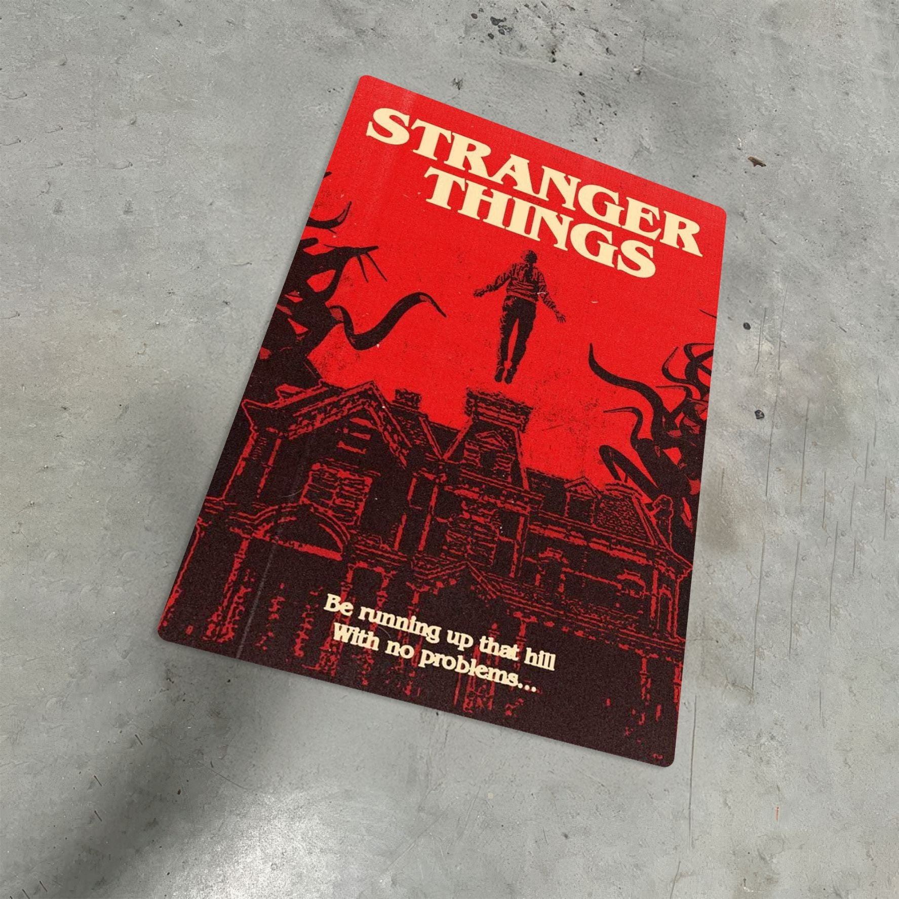 Max Mayfield Running Up That Hill metal poster with a vibrant red Stranger Things design displayed on a textured grey floor.