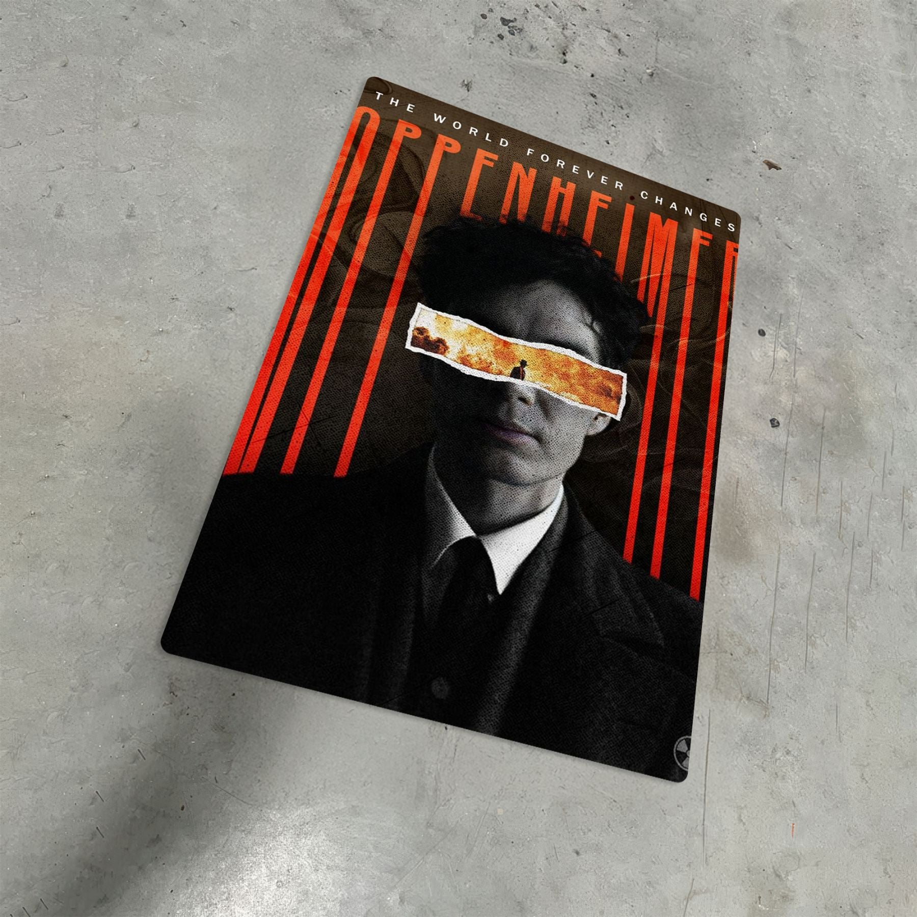 Oppenheimer Cillian Murphy movie metal poster on a textured grey floor showing a stylized portrait with a fire-filled eye strip.