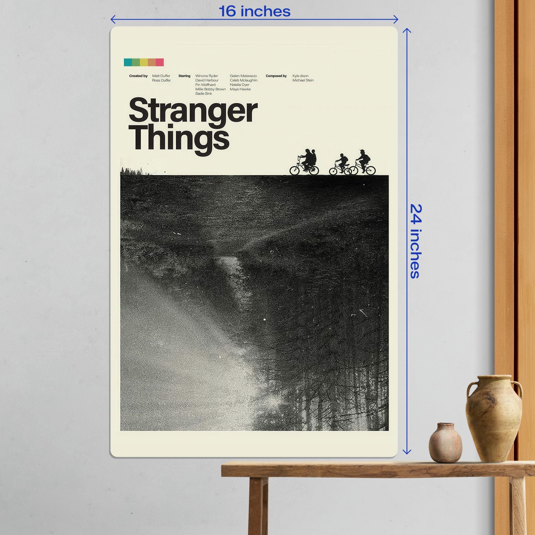 Large 16x24 inch Stranger Things kids on bikes metal poster shown as modern wall decor above a wooden table.